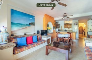 Una sala de estar con sofá, televisión y un cuadro de una playa.