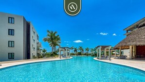 A swimming pool with clear blue water, surrounded by modern buildings and palm trees.