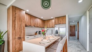 A modern kitchen with wooden cabinets, a central island with seating, and a stainless steel refrigerator.
