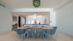 A modern dining area with a large rectangular table, six blue chairs, and a vase with flowers. - Paramount Bay PH 5 | 3BR/4BA Penthouse, PV | Ocean Views, Rooftop Pool (Puerto Vallarta)