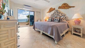 A bedroom with a large bed, a ceiling fan, decorative wall art, and a view of the outdoors.