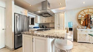 A modern kitchen with white cabinetry, a stainless steel refrigerator, a granite countertop, and a large island with bar stools.