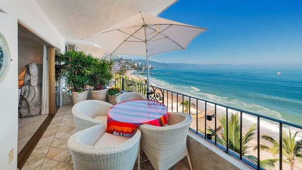 A balcony with wicker furniture, a striped table, and a beach view.