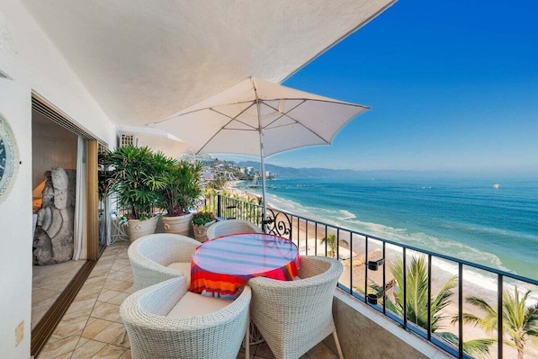 A balcony with wicker furniture, a striped table, and a beach view.