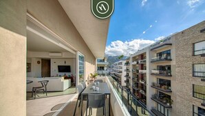 Een balkon met een eettafel en stoelen, met uitzicht op een woongebouw met balkons en een berg op de achtergrond.