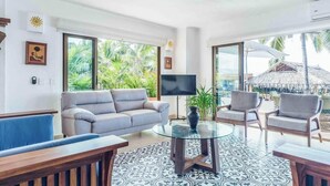 Ein Wohnzimmer mit einer Couch, Sesseln, einem Glastisch und einem Fernseher.