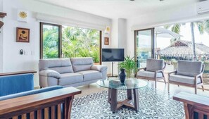 A living room with a sofa, chairs, a glass coffee table, and a TV. - Beachfront 2BR/2BA Condo with Spectacular Ocean Views, (Puerto Vallarta)