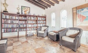 Ein geräumiger Lesesaal mit großen Bücherregalen, Korbsesseln und einem Schachbrettfußboden.