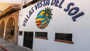 A building with a sign that reads 'VILLAS VISTA DEL SOL' and a colorful palm tree logo. - Puerto Vallarta 2BR/2BA | Beachfront Pool & Views (Puerto Vallarta)