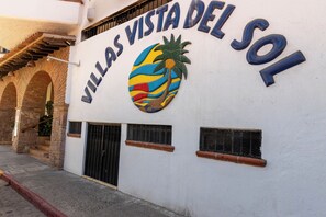 Een gebouw met een bord waarop 'VILLAS VISTA DEL SOL' staat, en een logo van een kleurrijke palmboom.