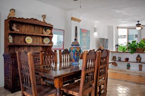 Een eethoek met een houten tafel en stoelen, een decoratieve houten kast met keramieken borden, en een kleurrijke keramieken vaas.