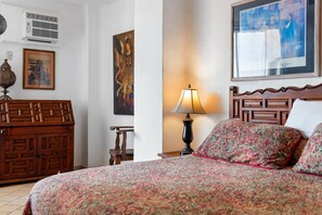 Ein Schlafzimmer mit einem Holz-Kopfteil, einem Bett mit gemusterten Betttextilien, einem Nachttisch mit Lampe und Bildern an den Wänden.