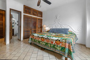 Une chambre à coucher avec un lit, un ventilateur de plafond, une porte en bois et une tête de lit fixée au mur.