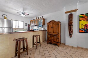 A kitchen with a refrigerator, wooden cabinets, a water dispenser, and a ceiling fan.