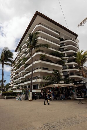 Un hôtel à plusieurs étages doté de balcons, de palmiers et d’une zone réservée aux vendeurs de rue.
