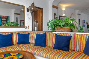 A vibrant, striped sofa with a large mirror and a potted plant in a room with white walls and wooden accents.