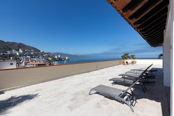 Eine Dachterrasse mit Liegestühlen, Blick auf das Meer und Gebäude im Hintergrund.