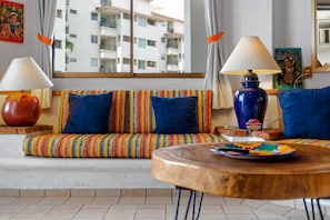 Una sala de estar con un sofá, dos lámparas, una mesa y vista a un edificio.