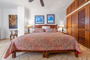 Un dormitorio con una cama grande, dos mesitas de noche con lámparas, un armario de madera y tres cuadros enmarcados en la pared.