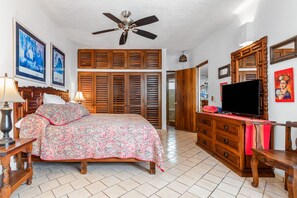 A bedroom with a bed, wooden wardrobe, ceiling fan, and a television.
