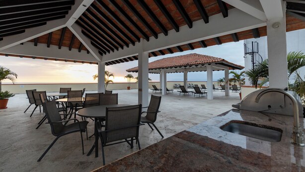 An outdoor patio with a grill, seating, and a view of the ocean. - Puerto Vallarta 2BR/2BA | Beachfront Pool & Views (Puerto Vallarta)