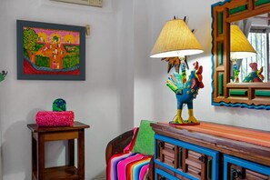 Ein Zimmer mit einem farbenfrohen Gemälde, einer Lampe mit dekorativem Sockel, einem Spiegel mit gewelltem Rahmen und einer Holzkommode mit Schubladen.