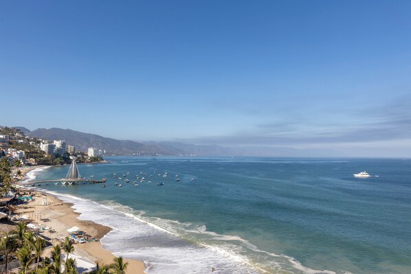 A coastal cityscape with a beach, a pier, and boats.