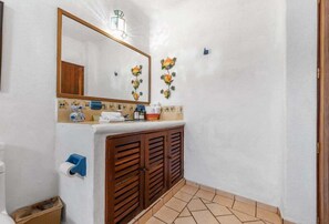 A bathroom with a mirror, wooden cabinets, a towel rack, and a trash bin.
