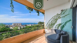 Een balkon met uitzicht op de stad, een grijze bank en een houten vloer.