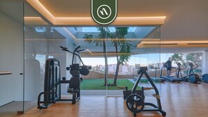 Een moderne sportschool met cardioapparatuur, krachttrainingsmachines en uitzicht op een groen buitengebied.