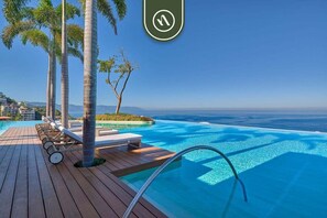 A poolside area with lounge chairs, palm trees, and a view of the ocean. - SoHo PV 806 | 1BR/2BA Puerto Vallarta | Beach, Pool, Gym (Puerto Vallarta)
