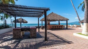 Terrassa al costat de la platja amb una barbacoa, ombrel·les de palla i zona de bar.