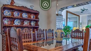 A dining area with a wooden table and chairs, a decorative shelf with plates, and a large vase.