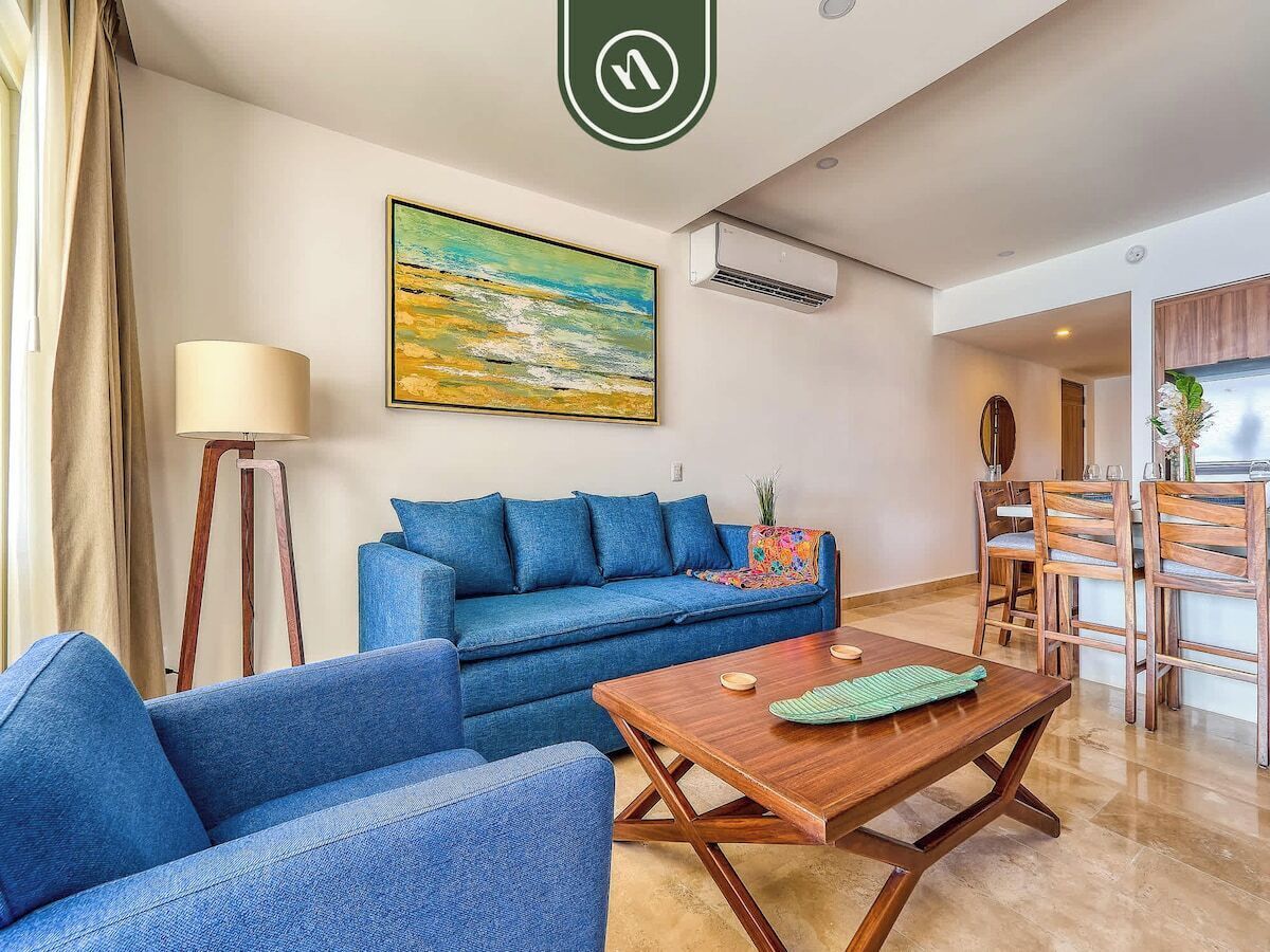 Una sala de estar con un sofá azul, una mesa de centro de madera y un cuadro en la pared.