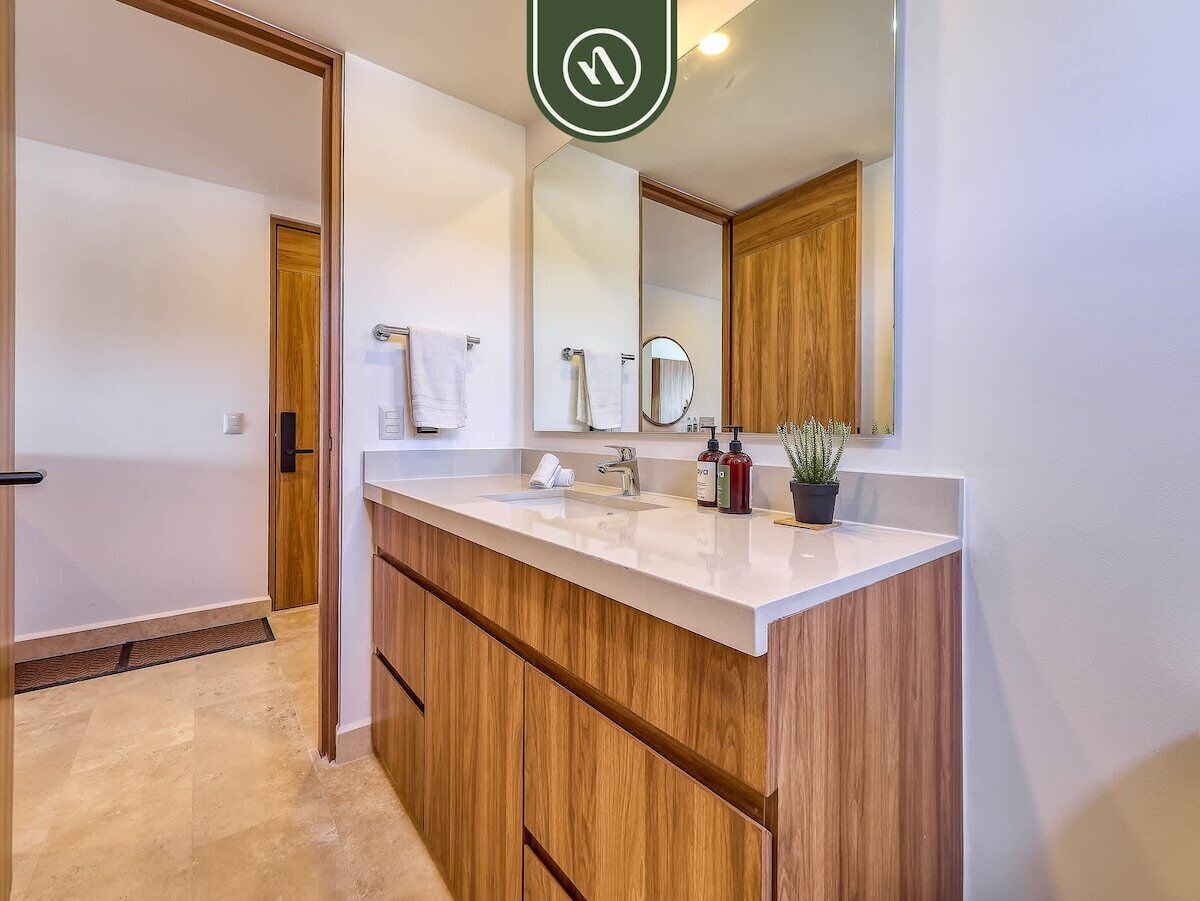 Un baño moderno con tocador de madera, un espejo grande y una planta en maceta.