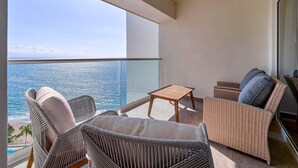A balcony with wicker furniture, a small table, and a view of the ocean.