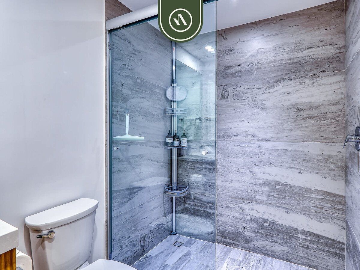 Un baño moderno con ducha envuelta en vidrio, inodoro y salpicadero de mármol.