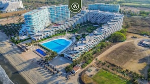 A large hotel with multiple buildings, a swimming pool, and a beach area.