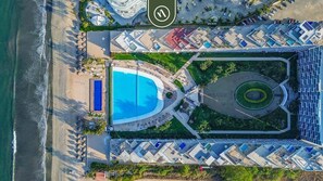 Vue aérienne d’un complexe hôtelier doté d’une piscine, de chaises longues et d’un espace paysager.