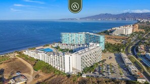 Um hotel grande com vários andares, piscina e vista para o mar.