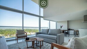 Una sala de estar moderna con un ventanal grande, un sofá gris, una mesa de centro de madera y un área de comedor con mesa y sillas.