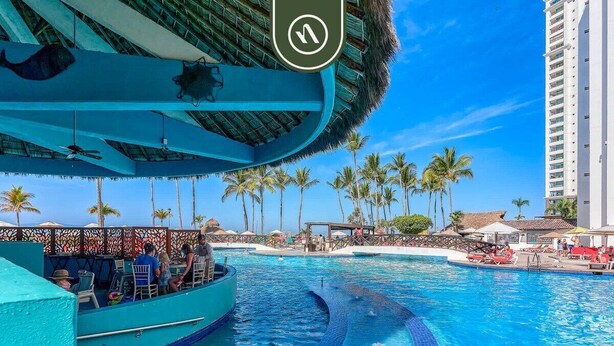 Zona de piscina con un barco, palmeras y un edificio alto al fondo.