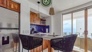 Una cocina moderna con un refrigerador de acero inoxidable, armarios de madera, un respuesto de azulejos azules y un comedor con dos sillas negras.