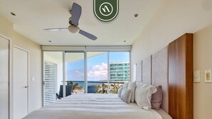 Un dormitorio con una cama grande, un ventilador de techo y vista al océano a través de una puerta corrediza.