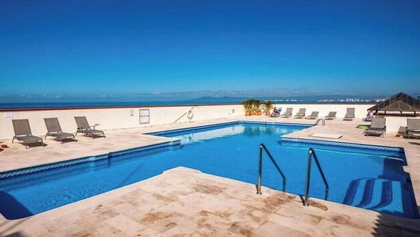 A rooftop pool with lounge chairs, a small pavilion, and a view of the ocean. - 206-VistadelSol | 2BR/2BA Ocean View, Beachfront (Puerto Vallarta)