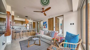 A modern living room with a sofa, coffee table, and wicker chair. There is a kitchen in the background with bar stools. - Serenity 301 | 2BR Puerto Vallarta | Rooftop Pool (Puerto Vallarta)