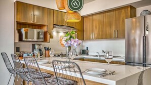 A modern kitchen with wooden cabinets, a stainless steel refrigerator, a built-in microwave, and a marble island with bar stools. - Serenity 301 | 2BR Puerto Vallarta | Rooftop Pool (Puerto Vallarta)