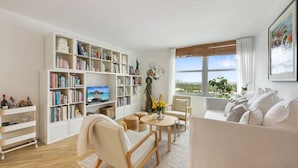 A spacious living room with a large bookshelf, a comfortable sofa, a coffee table, and a view of the outdoors through a large window. - Charming 1-bedroom condo in the heart of  Miami Beach (Miami)