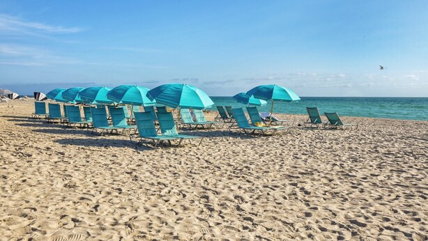 A beach with rows of blue sun loungers and umbrellas, a clear sky, and the ocean in the background. - Charming 1-bedroom condo in the heart of  Miami Beach (Miami)