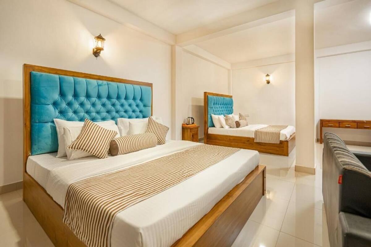 A hotel room with two beds, each with a tufted headboard, a wooden bench, and a small bedside table.